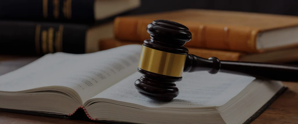 A judge's gavel rests on an open law book, with closed books in the background.