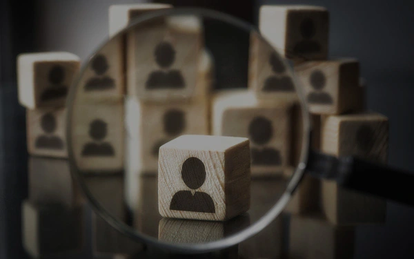 Wooden blocks with silhouette icons of people, one block enlarged under a magnifying glass.