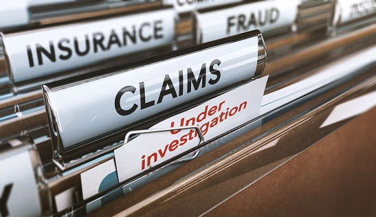 Close-up of file folders labeled "Claims" and "Under Investigation," with other categories like "Insurance" and "Fraud" visible in the background.