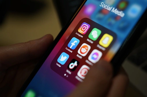 A person holds a smartphone displaying various social media app icons, including Instagram, Facebook, and Twitter.