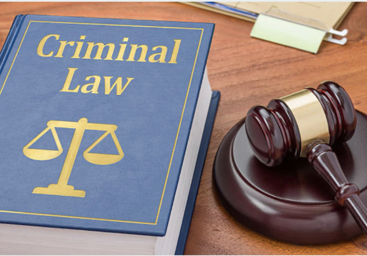 A criminal law book with a blue cover sits beside a wooden gavel on a desk.