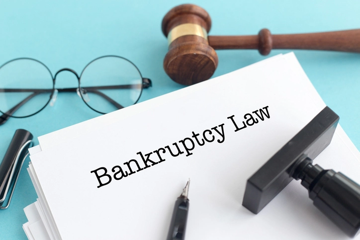 A stack of papers labeled "Bankruptcy Law" with a gavel, glasses, a pen, and a stamp on a blue background.